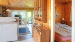 Une chambre confortable, aménagée dans le style d’un chalet, avec un plafond en bois, un lit doté d’un matelas rose, une armoire en bois, une télévision et une petite table avec une lampe.