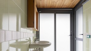 A modern bathroom with a glass sink, wooden ceiling, and a view through a sliding door.