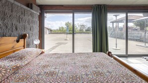 A bedroom with a bed, a wooden headboard, a stone wall, and a large window with a view of an outdoor area.