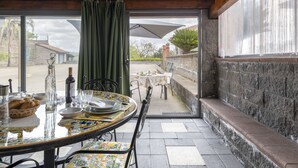 An outdoor dining area with a round table set for two, a green curtain, and a stone wall.