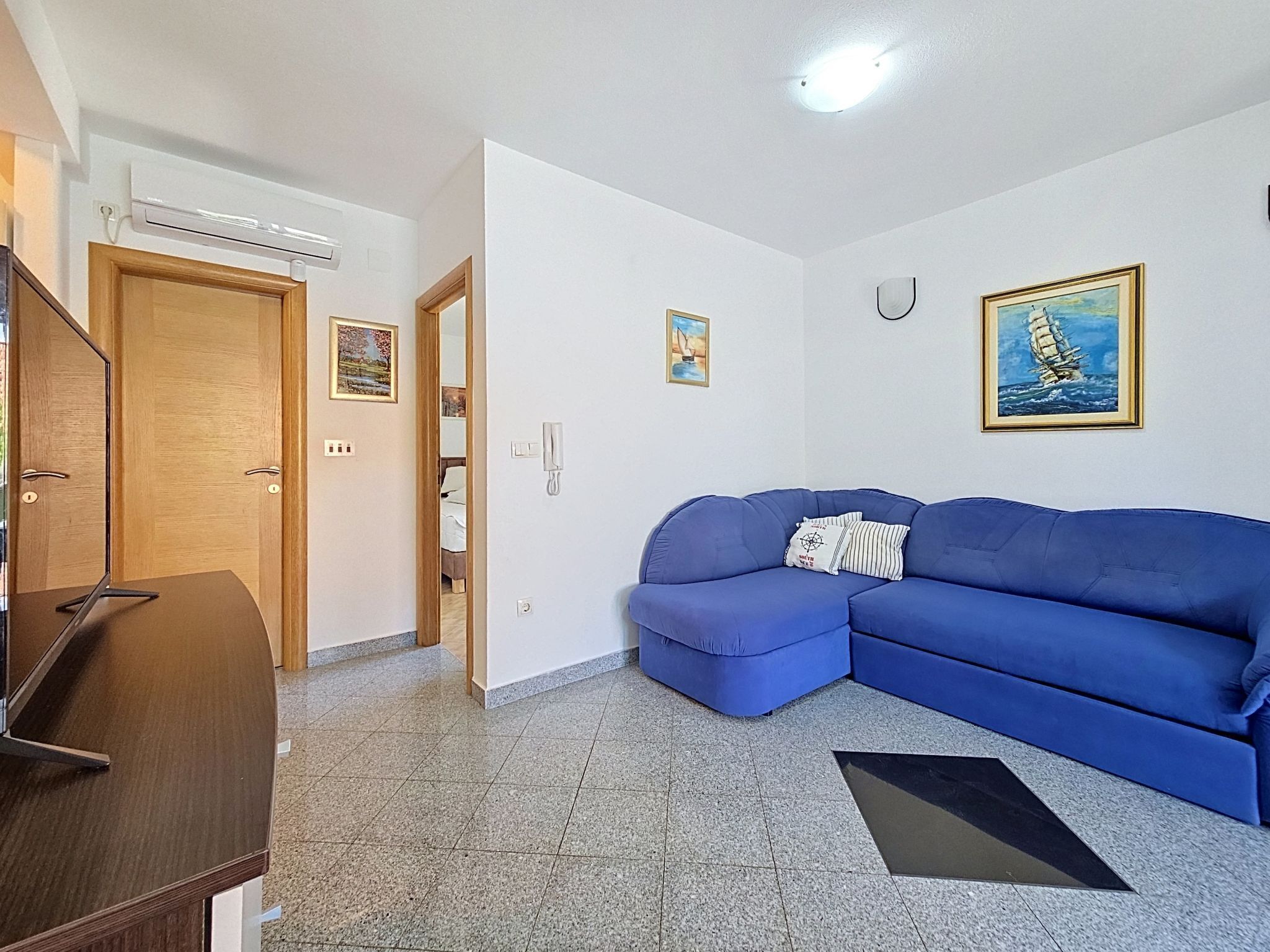 A living room with a blue sofa, a wooden door, a small table, and a painting on the wall.