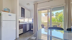 A modern kitchen with a refrigerator, microwave, and cabinets, leading to a balcony with a glass table and chairs. - Apartment Marko by Interhome (Zadar/Bibinje)