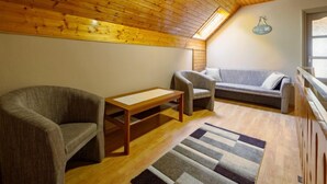A cozy loft bedroom with a sloped ceiling, wooden beams, a sofa, two armchairs, a small table, and a welcome sign. - Apartment Swing by Interhome (Balatonszarszo)
