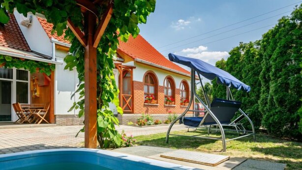 A swimming pool with a wooden pergola and a covered chair, a brick building with arched windows, and a well-maintained garden. - Apartment Swing by Interhome (Balatonszarszo)