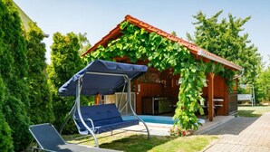 A covered outdoor seating area with a swing chair, a pool, and a wooden structure with vines. - Apartment Swing by Interhome (Balatonszarszo)