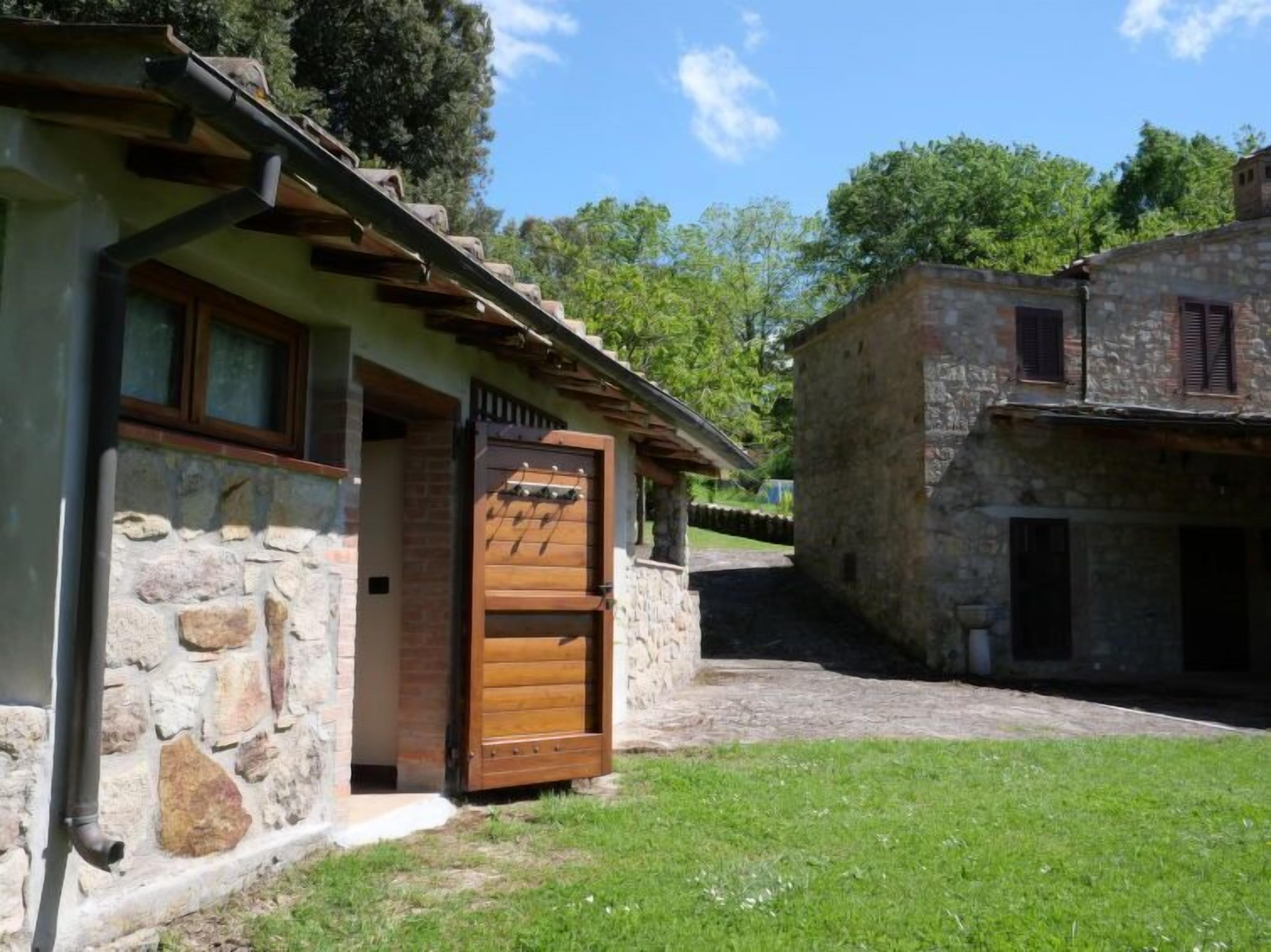 A stone building with a wooden door, a stone wall, and a grassy area.