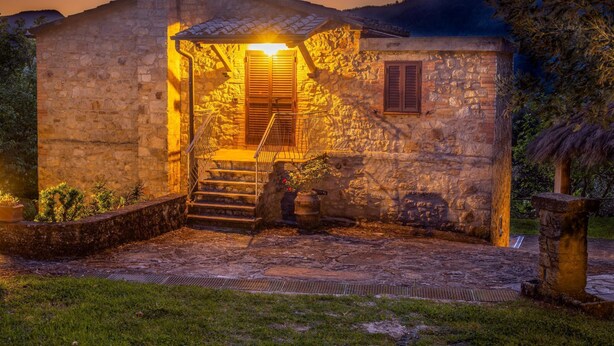 Un bâtiment en pierre avec un escalier menant à une porte en bois, le tout entouré de verdure.