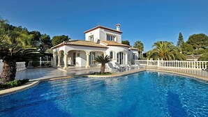 Une grande villa blanche dotée d’une piscine, entourée de palmiers et d’une clôture blanche.