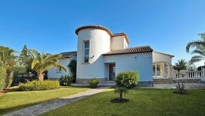 Une maison à deux étages, dotée d’un coin arrondi, d’un toit recouvert de tuiles et d’une pelouse bien entretenue agrémentée de petits arbres.
