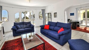 Un salon spacieux avec deux canapés bleus, une table basse en verre et un tapis rouge.