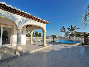 Ein überdachter Patio-Bereich mit Swimmingpool, Palmen und blauem Himmel.