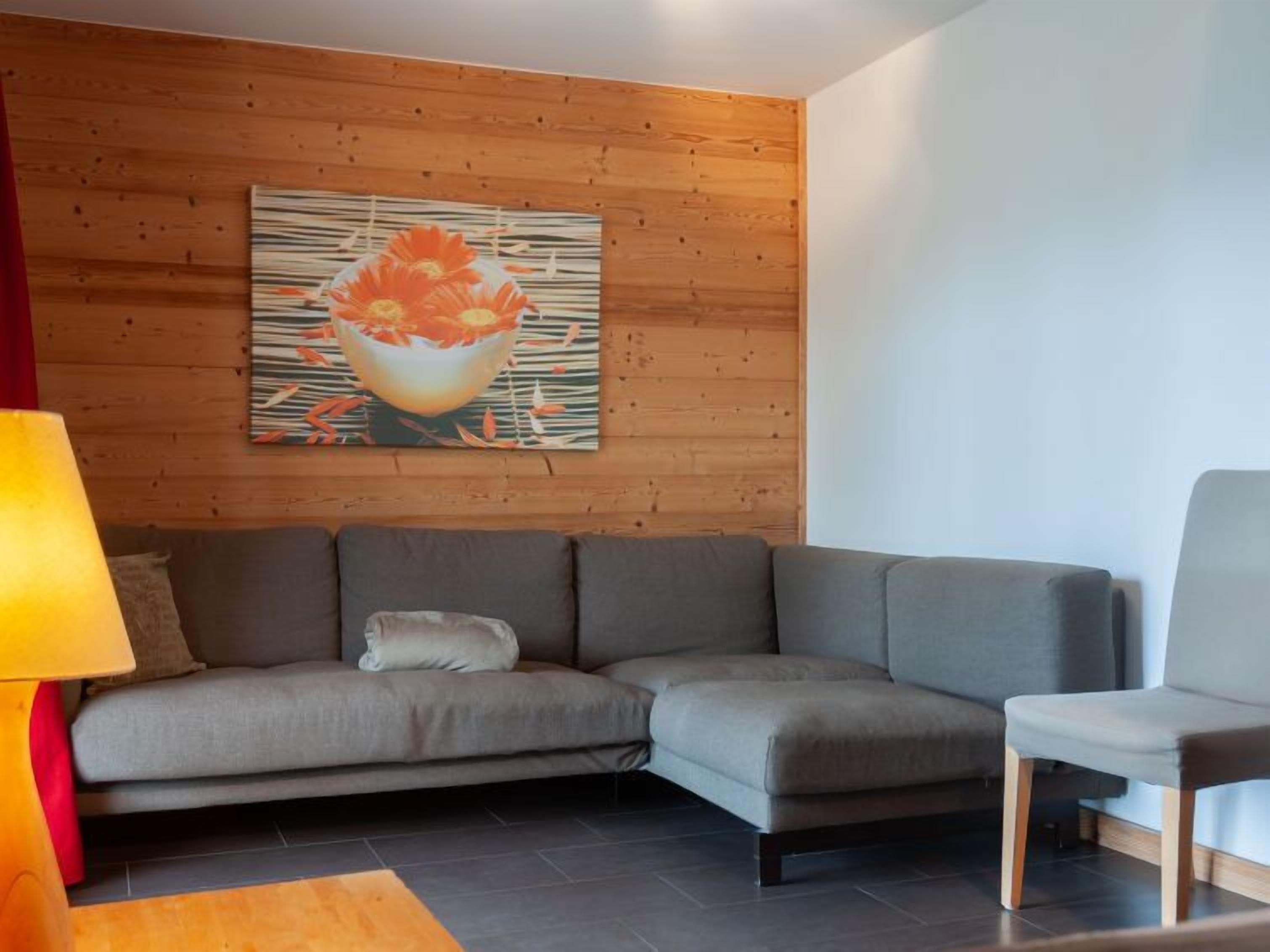 A modern living room with a grey sectional sofa, a wooden wall, and a painting of flowers.