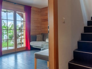 A room with a large sliding glass door leading to a balcony, a wooden interior, a sofa, and a staircase.