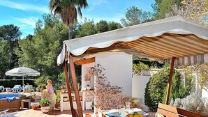 Eine Terrasse im Freien mit Holzmöbeln, einer überdachten Sitzgelegenheit und einem Pool im Hintergrund.