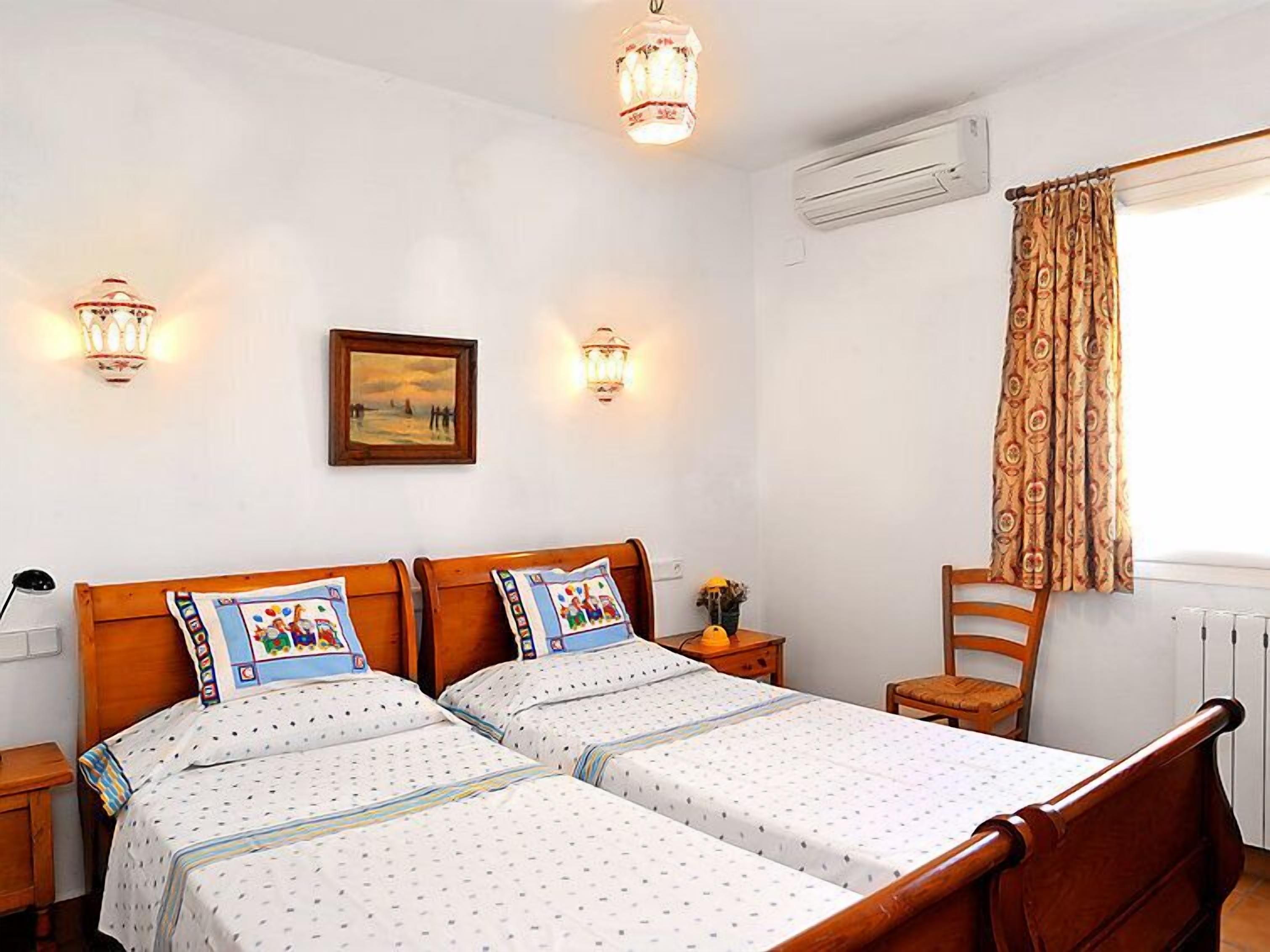 A double room with two single beds, a wooden headboard, a bedside table with a lamp, a framed picture on the wall, and a window with curtains.