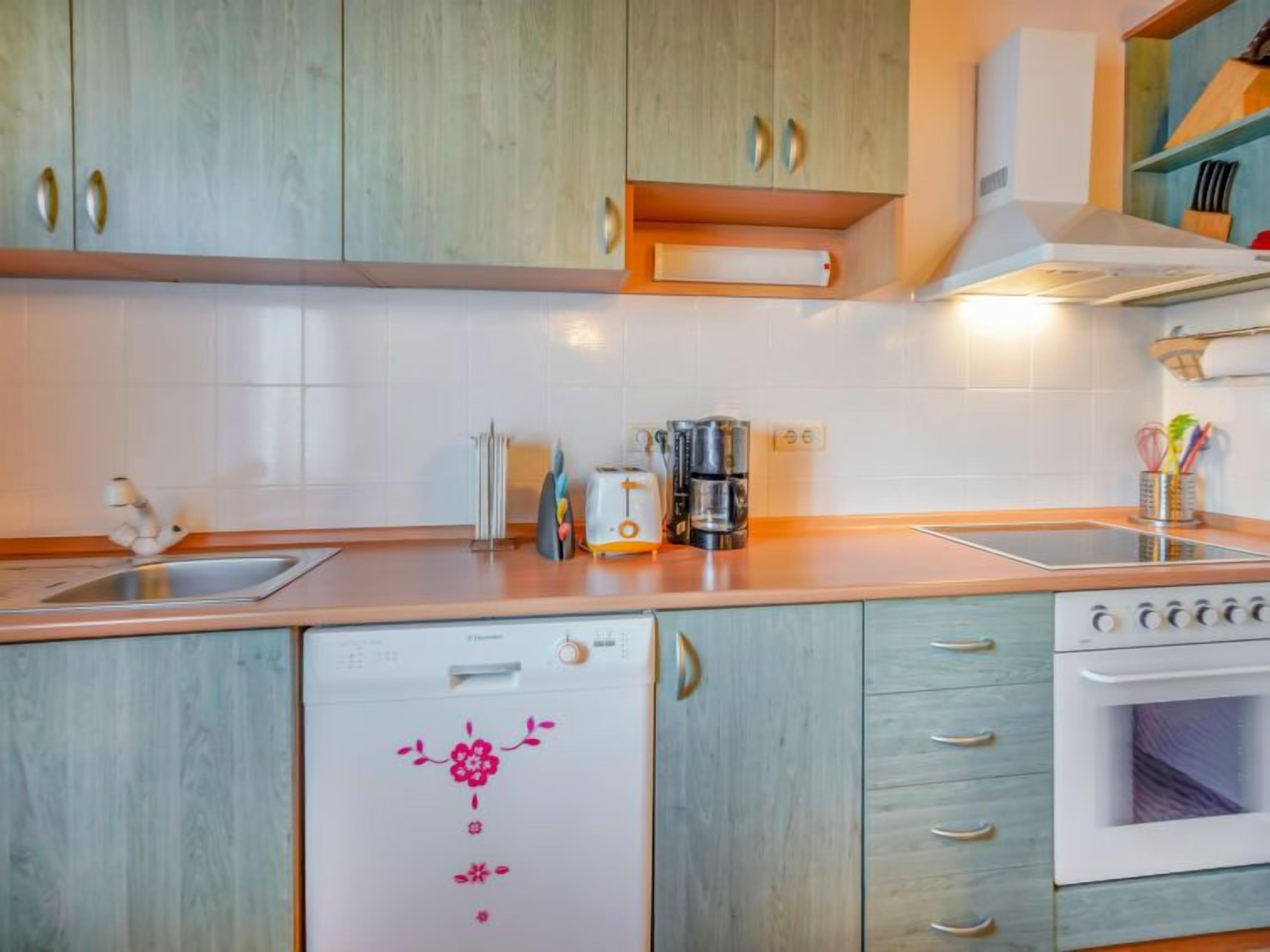 A compact kitchen with wooden cabinets, a built-in oven, a dishwasher, and a coffee maker.