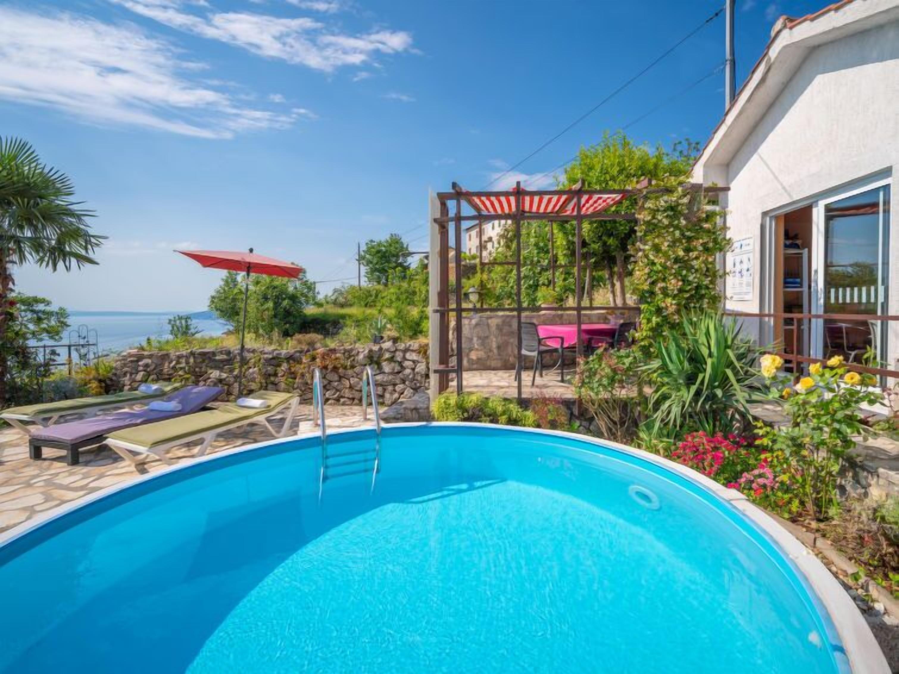 Une piscine dotée de chaises longues et d’une pergola, entourée de verdure et d’un mur de pierre.
