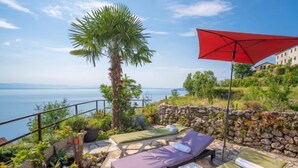 Una terraza con dos sillones, una sombrilla roja y vista al mar.