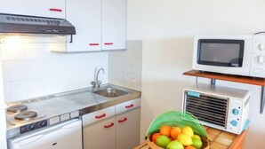 A compact kitchen with white cabinets, a stainless steel sink, a stove, a microwave, and a toaster. A basket of fruit is on the counter. - Zirlinga by Interhome (Bidart)