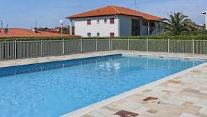 A swimming pool with a tiled deck, surrounded by a white fence and a building with a red roof in the background. - Zirlinga by Interhome (Bidart)