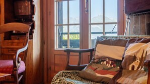 Een gezellige kamer met houten meubels, een groot raam met uitzicht op bergen, en een gestreept kussen op een stoel.