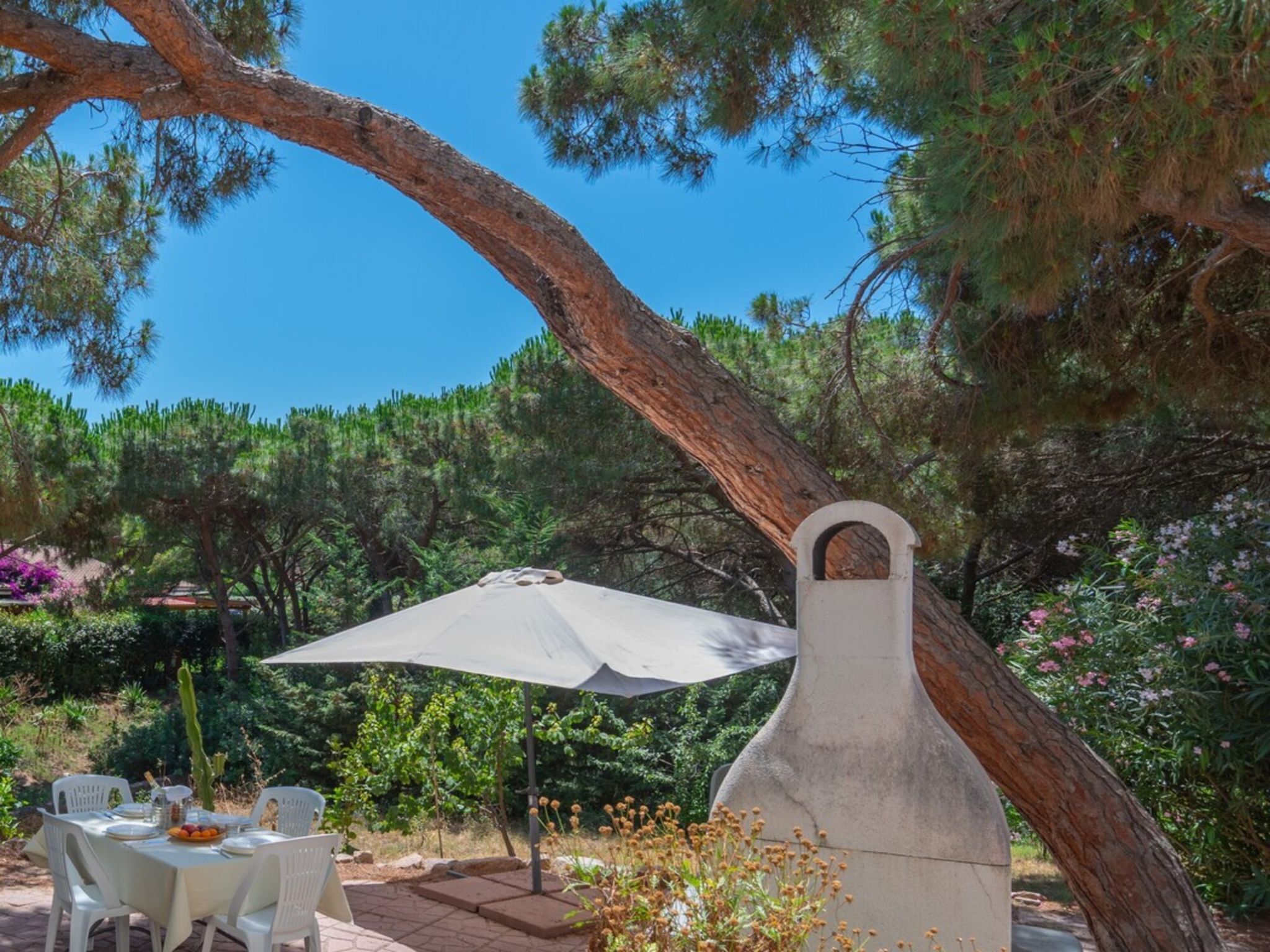 Un'area pranzo all'aperto con tavolo e sedie, un ombrellone grande e una struttura in pietra particolare.