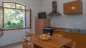 Eine Küche mit Holztisch, Stühlen, einem Herd, einer Spüle und einem Fenster mit Blick ins Grüne.