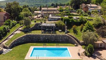 Una piscina con un ponte in pietra, lettini da relax e un muro di pietra.