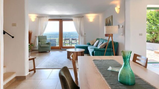 Uma sala de estar espaçosa com uma grande porta de vidro deslizante que dá para uma varanda, um sofá verde, uma mesinha redonda e um vaso verde sobre uma mesa de madeira.