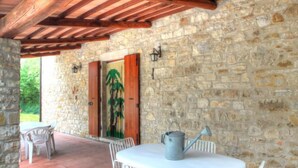 A stone-walled patio with a table and chairs, a wooden ceiling, and a door with a green door knocker. - Torregentile by Interhome (Todi)