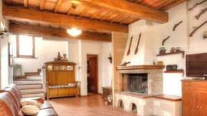 A cozy living room with a leather sofa, a fireplace, wooden beams, and a staircase. - Torregentile by Interhome (Todi)