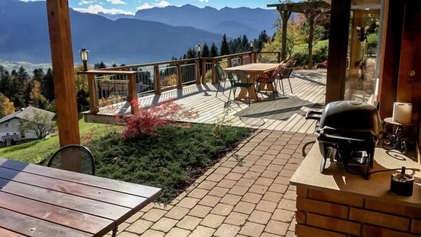 A wooden deck with a table and chairs, overlooking a mountainous landscape.