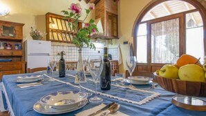 Un coin repas avec une table dressée pour quatre personnes, agrémenté de nappes bleues, d’assiettes blanches et de verres transparents. Un vase rempli de fleurs et quelques bouteilles sont posés sur la table.