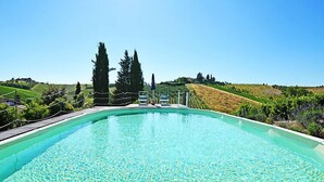 Une piscine d’un bleu éclatant, dotée d’une terrasse en bois et entourée de verdure et de collines.