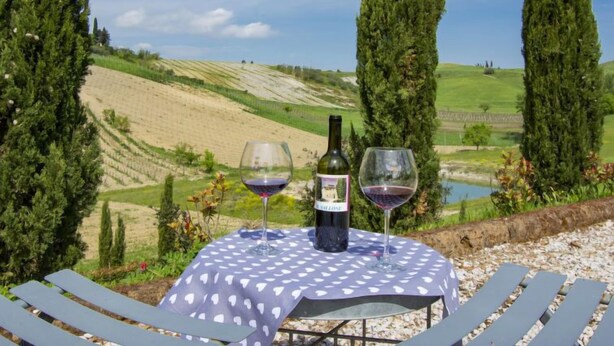 Une table avec une bouteille de vin et deux verres, placée devant un paysage pittoresque de colline.