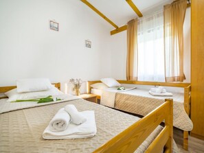 A hotel room with two beds, wooden headboards, a window with sheer curtains, and a small vase with dried flowers on the nightstand. - Vacation home Jozo by Interhome (Omiš)