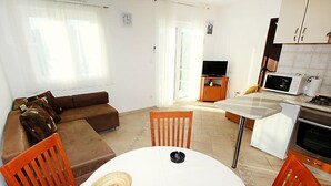 A compact living space with a sofa, dining table, chairs, a kitchen area with appliances, and a television. - Parunov by Interhome (Šolta/Rogac)