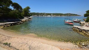 A clear coastal view with boats docked near a rocky shoreline and a distant village. - Parunov by Interhome (Šolta/Rogac)