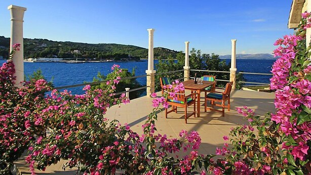 A terrace with a table and chairs overlooking a body of water, surrounded by pink flowers and greenery. - Parunov by Interhome (Šolta/Rogac)