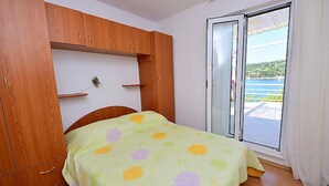 A bedroom with a bed, wooden wardrobe, and a sliding glass door leading to a balcony. - Parunov by Interhome (Šolta/Rogac)