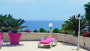 Zona junto a la piscina con vistas al mar, un farol blanco y una tumbona rosa.
