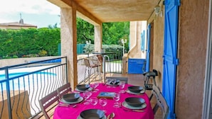 Comedor con mesa preparada para seis personas, con vista a una piscina y follaje.