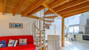 Un intérieur moderne avec un canapé rouge, une chaise blanche, un escalier en colimaçon en bois et un coin cuisine.