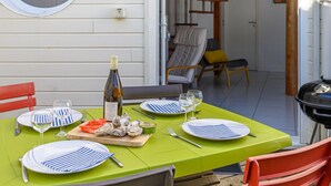 Un espace de restauration en plein air avec une table verte dressée pour quatre personnes, agrémentée d’assiettes à rayures et d’une bouteille de vin.
