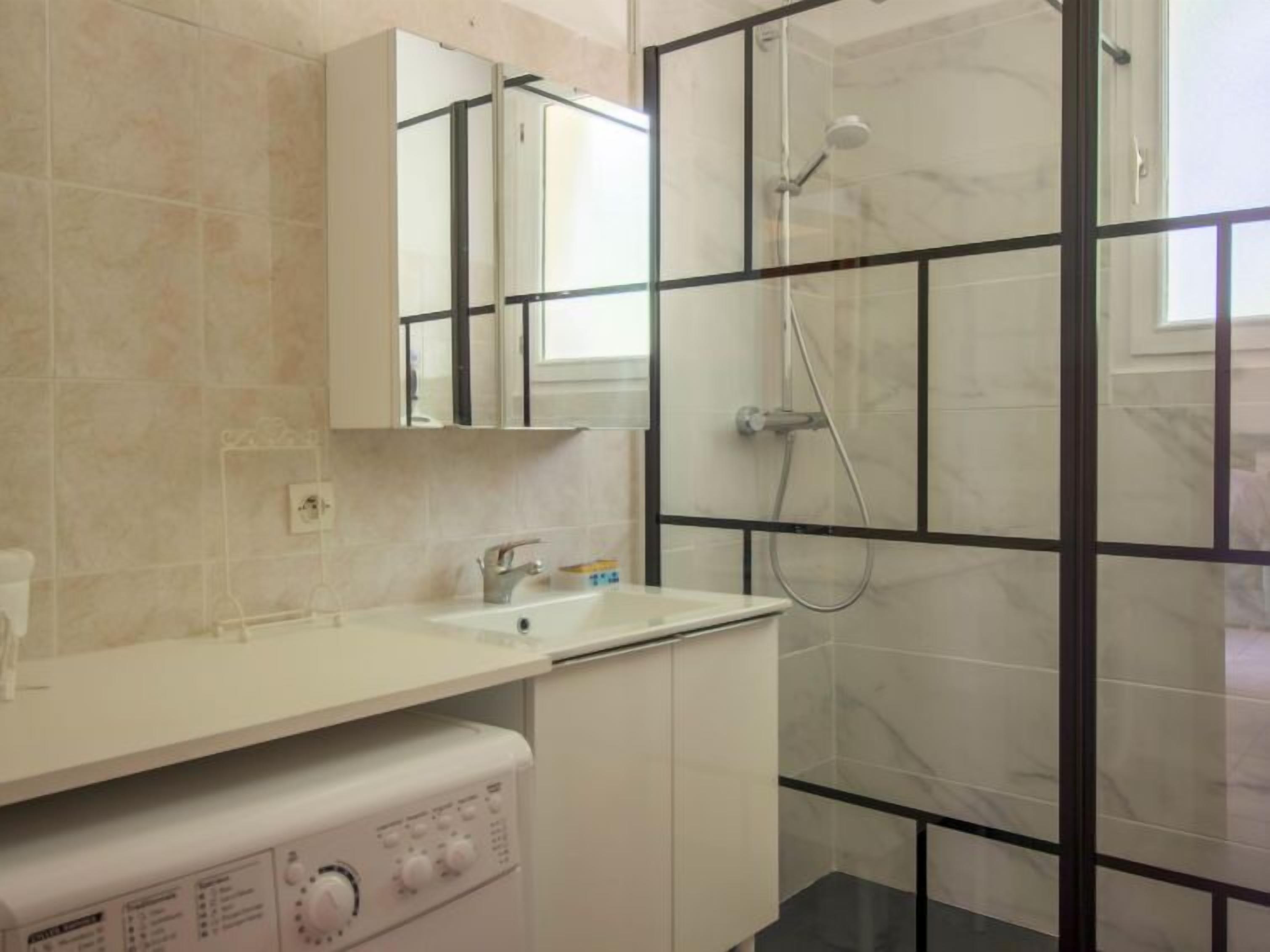 Un baño con lavamanos blanco, espejo, ducha con mampara de vidrio y lavadora.