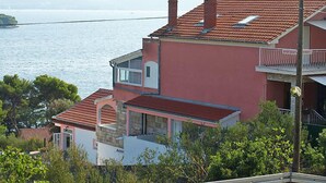 En bostadsbyggnad vid kusten med ett rött tegeltak, en balkong och utsikt över havet.