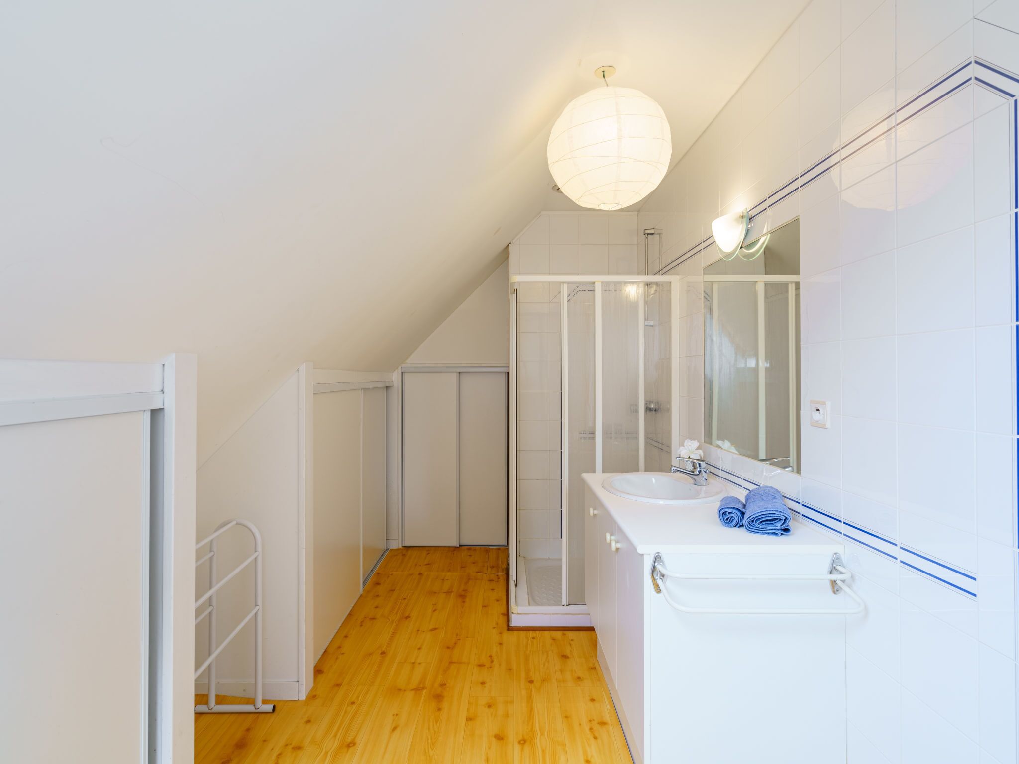 Un baño moderno con suelo de madera, muebles blancos y un espejo grande, además de un lavabo blanco.