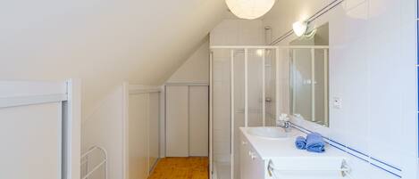 Un baño moderno con suelo de madera, muebles blancos y un espejo grande, además de un lavabo blanco.