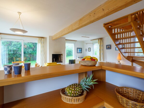A wooden dining table with a pineapple and a fruit basket, a staircase, and a view of the outdoors.