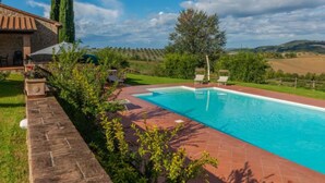 Una piscina con terraza de piedra, rodeada de vegetación y vistas a colinas ondulantes.